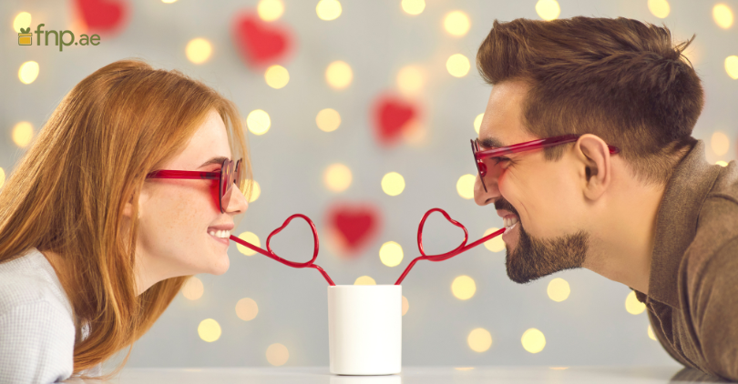 Beautiful Couple enjoying their drinks together through a heart shaped straw dipped in glass