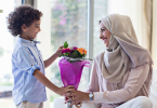 A cute boy giving yellow flower bouquet to his mother