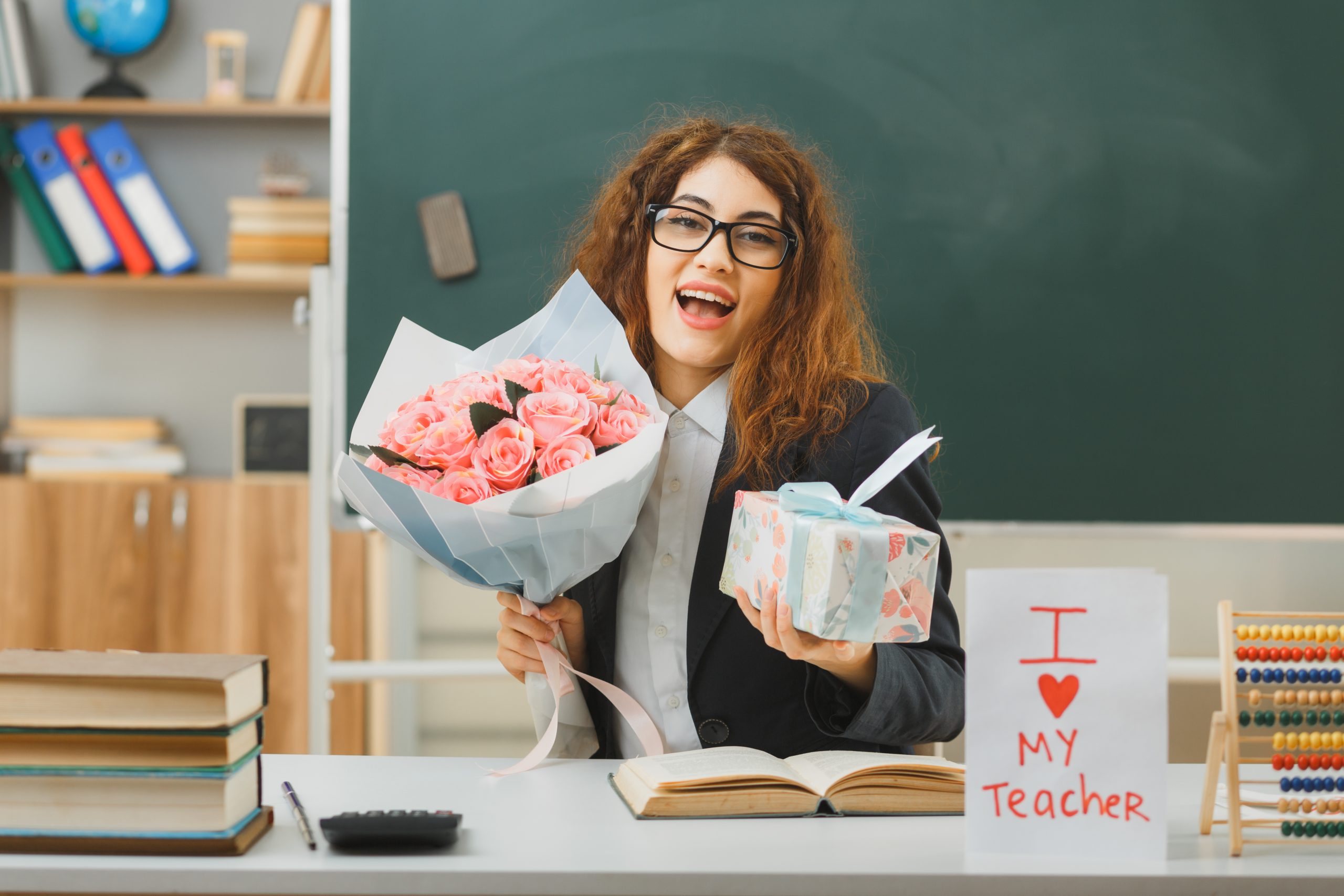 Female Teacher holding pink rose bouquet and personalised gift in her hands presented by her students